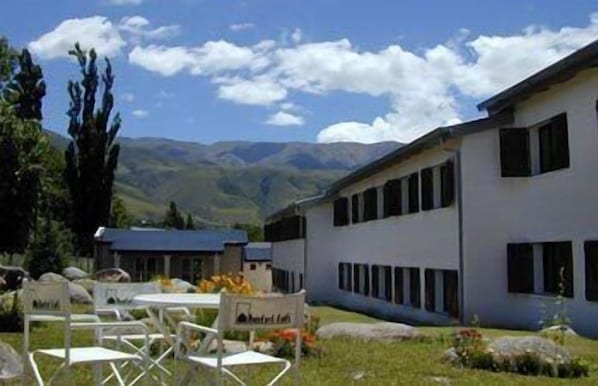 Un edificio de fachada blanca y varias ventanas, rodeado de césped con algunas sillas y una mesa.
