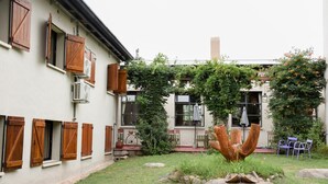 A courtyard with a white building featuring wooden shutters, a rock garden, and a unique sculpture. - Hotel Tafi (Tafi del Valle)