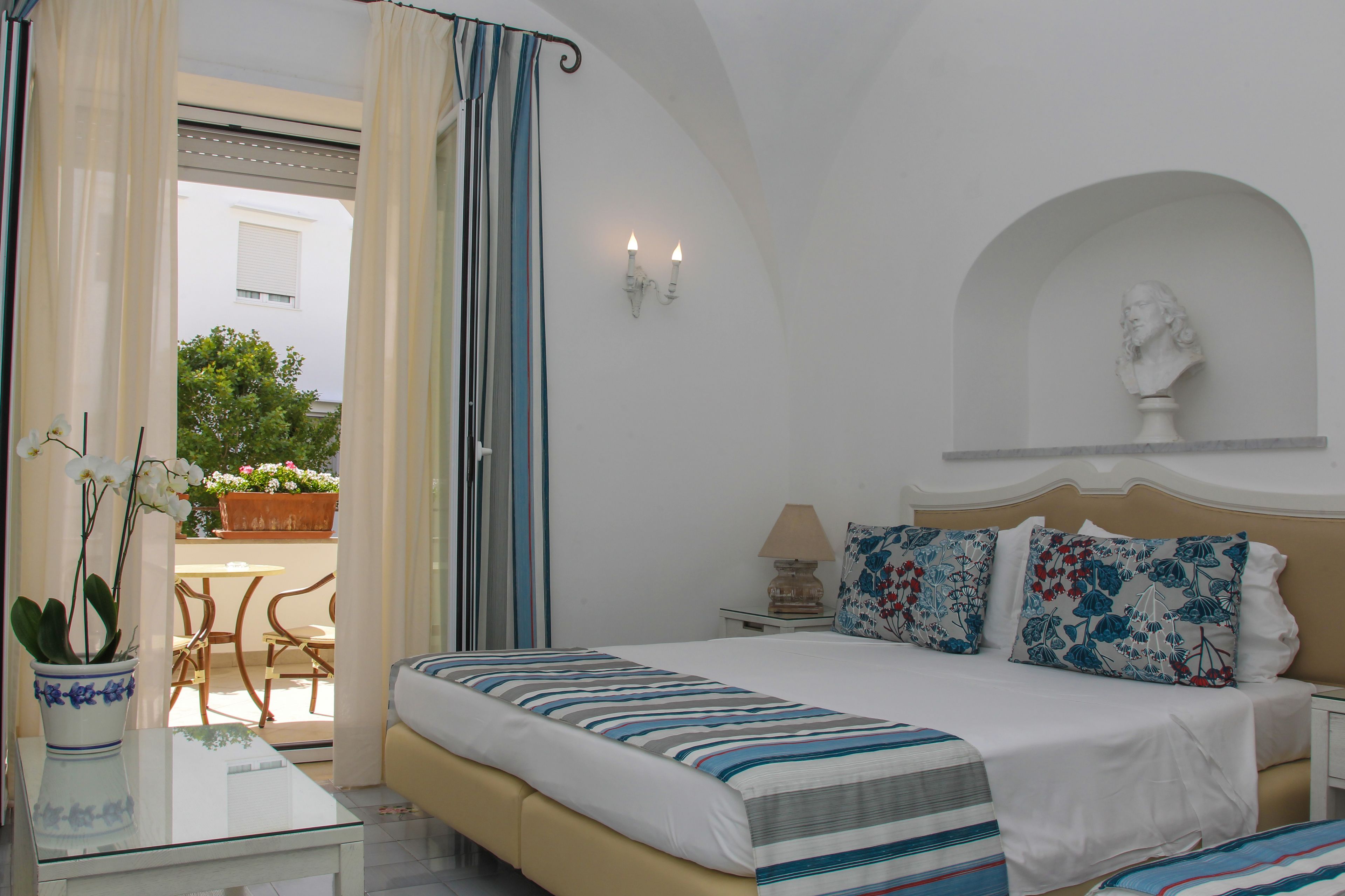 Ein Hotelzimmer mit Bett, Nachttisch, Lampe und einer Büste an der Wand.