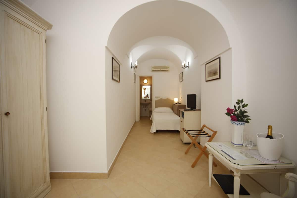 A hallway leading to a bedroom with a bed, a table with a vase of flowers, and a bottle of champagne.