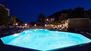 A nighttime swimming pool with lounge chairs and umbrellas, surrounded by buildings and palm trees. - Villa San Felice (Capri)