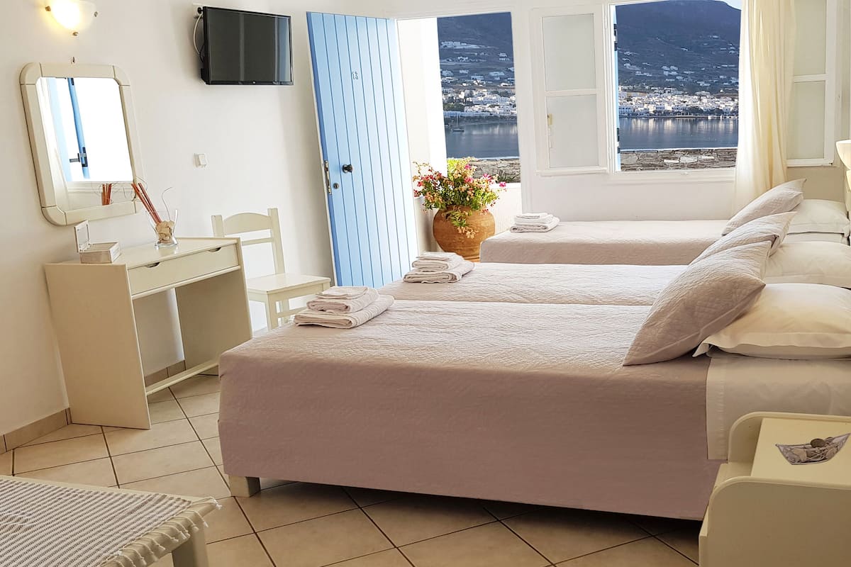 A hotel room with two beds, a desk, a chair, a TV, and a view of the sea.