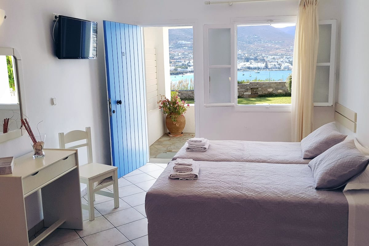 A hotel room with two beds, a desk, a chair, a TV, and a view of the sea.