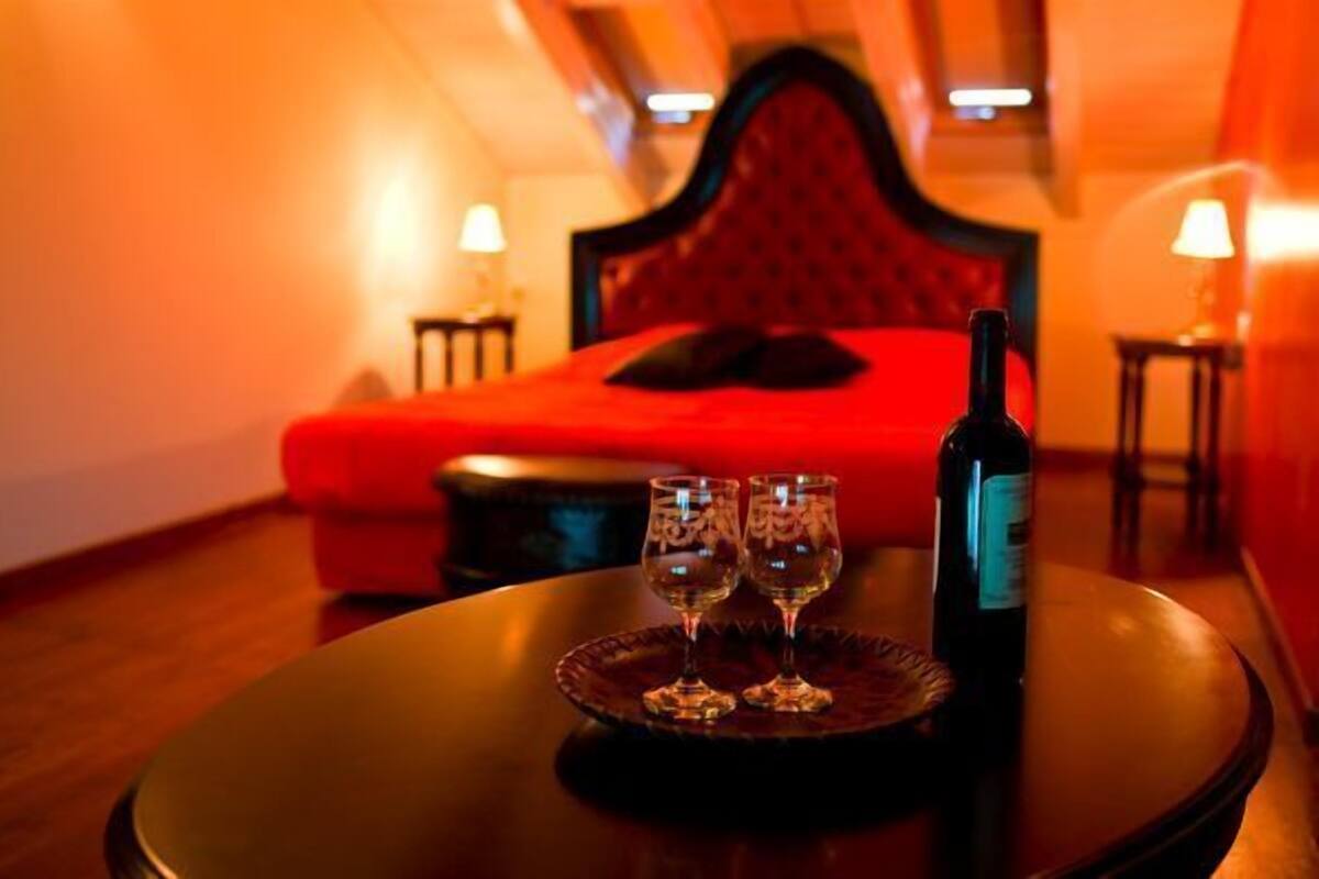 A hotel room with a red bed, a bottle of wine, and two glasses on a table.