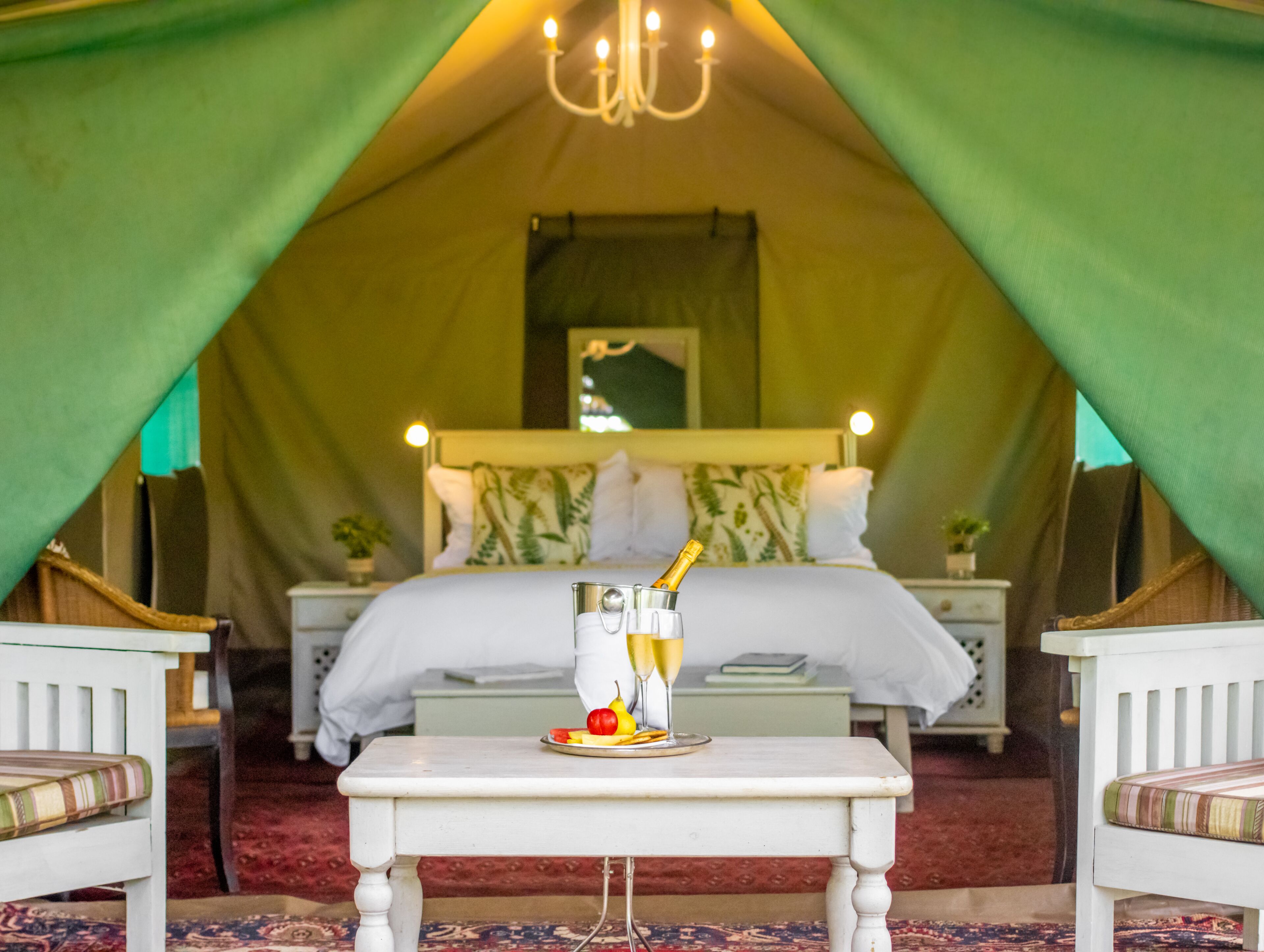 A tented room with a bed, a table with a bottle and glasses, and a chandelier.