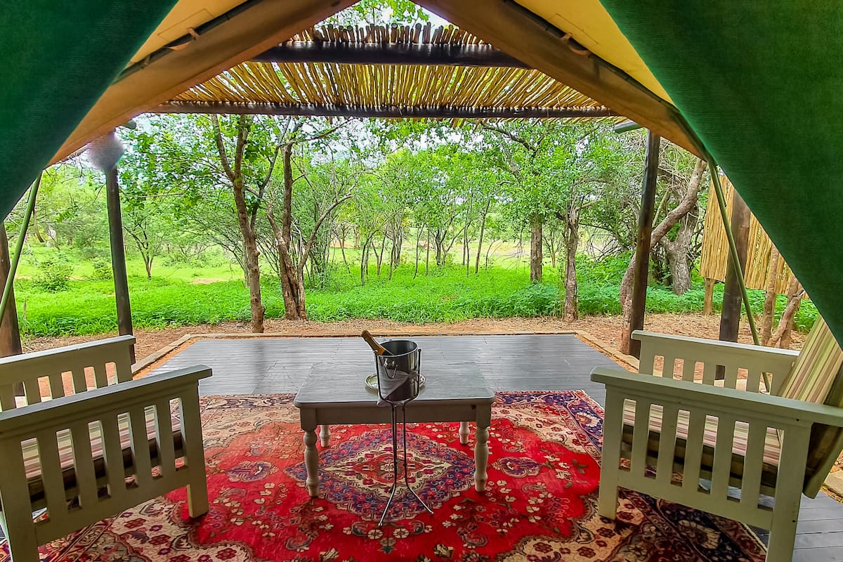 Ein Sitzbereich im Freien mit Tisch und Stühlen, einem gemusterten Teppich und Blick auf eine grüne Landschaft.