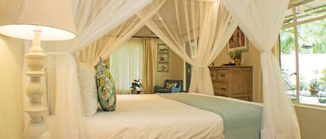 A bedroom with a bed, a bedside lamp, a chair, a dresser, and a window with curtains.