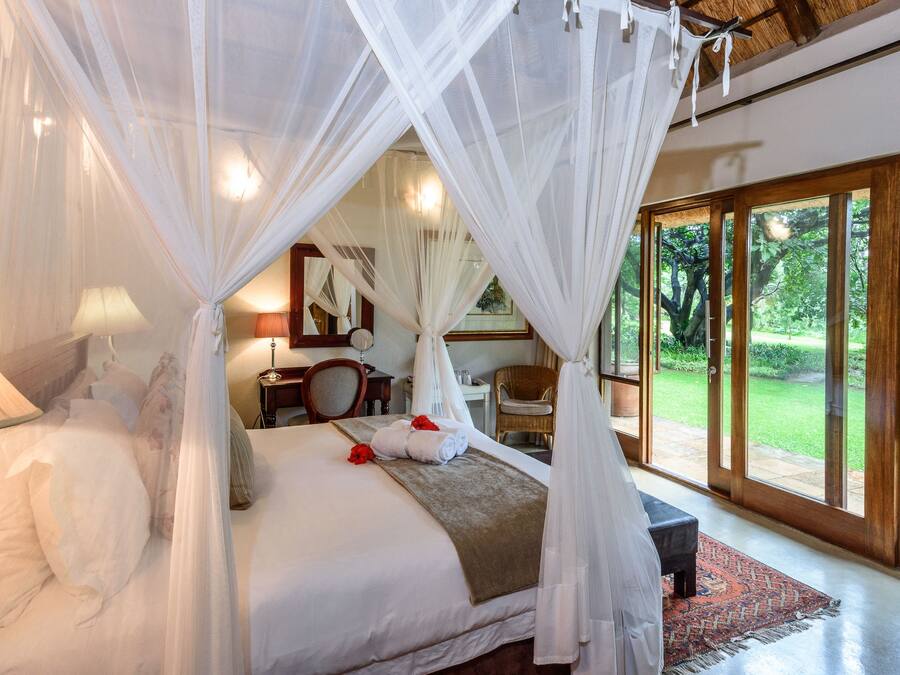 Un dormitorio espacioso con una cama grande, dosel y vistas a un jardín exuberante a través de amplios ventanales.