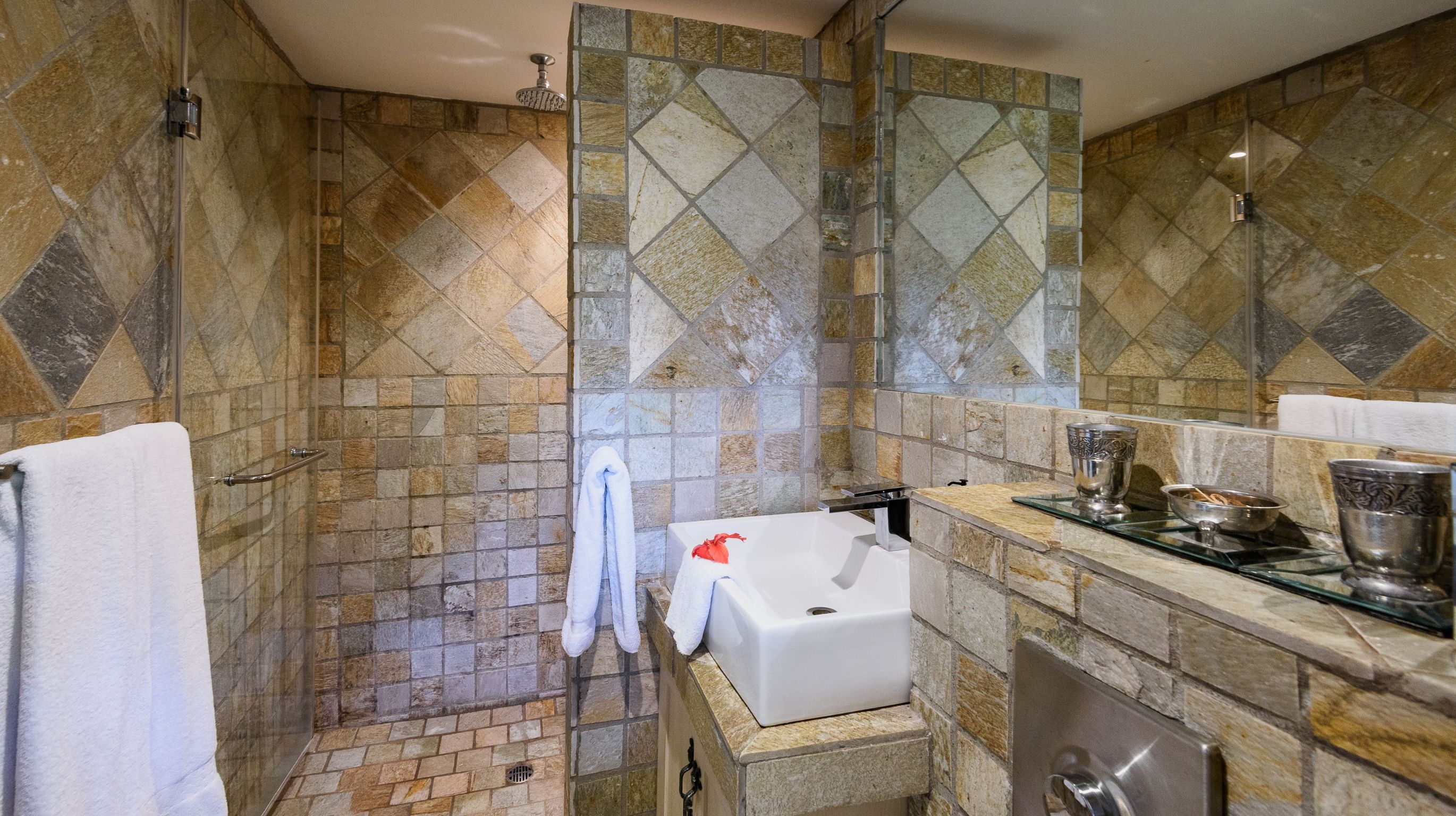 A bathroom with stone tile walls, a bathtub, a shower, and a sink with a glass countertop.