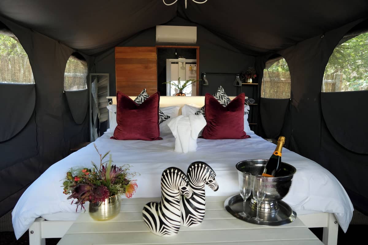Ein Zelttyp-Zimmer mit einem Bett, Kissen, einer Blumenvase und einer Champagnerflasche.