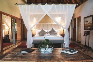 Ein Schlafzimmer mit Baldachinbett, Nachttisch mit Büchern und einer Zimmerpflanze.