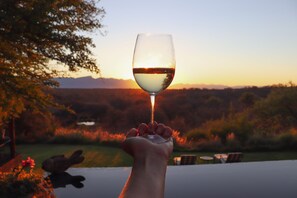 Eine Hand, die ein Weinglas hält, mit Blick auf einen Sonnenuntergang im Hintergrund.