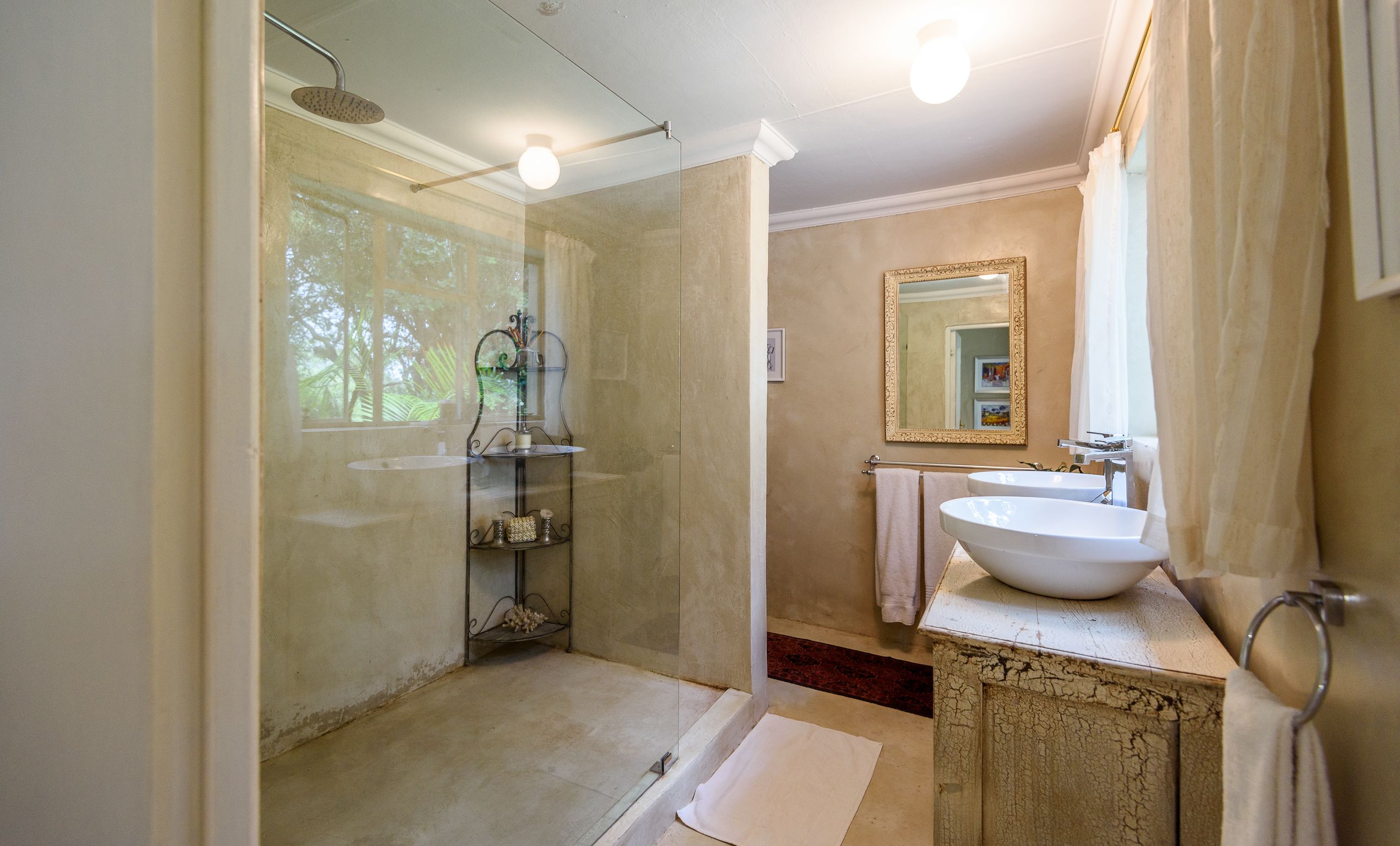A bathroom with a glass-enclosed shower, a sink with a decorative cabinet, and a mirror with a gold frame.