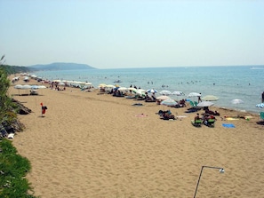 Una playa con hileras de sombrillas y sillas reclinables, una bandera y gente nadando en el agua.