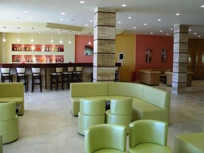 A lobby with a bar area, seating arrangements, and a stone pillar. - Golden Sands Hotel (Corfu)