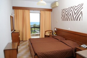 A hotel room with a bed, a chair, a desk, a mirror, and a view of the sea. - Golden Sands Hotel (Corfu)