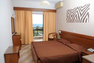 Una habitación de hotel con cama, una silla, un escritorio, un espejo y vista al mar.