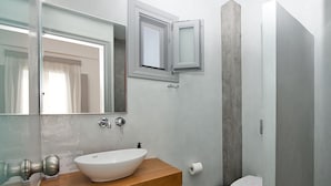 Un baño moderno con tocador de madera, un lavamanos blanco, un espejo, inodoro y zona de ducha.