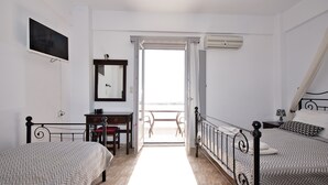 Un dormitorio con dos camas, un escritorio, una silla, un televisor y un balcón con mesa y sillas.