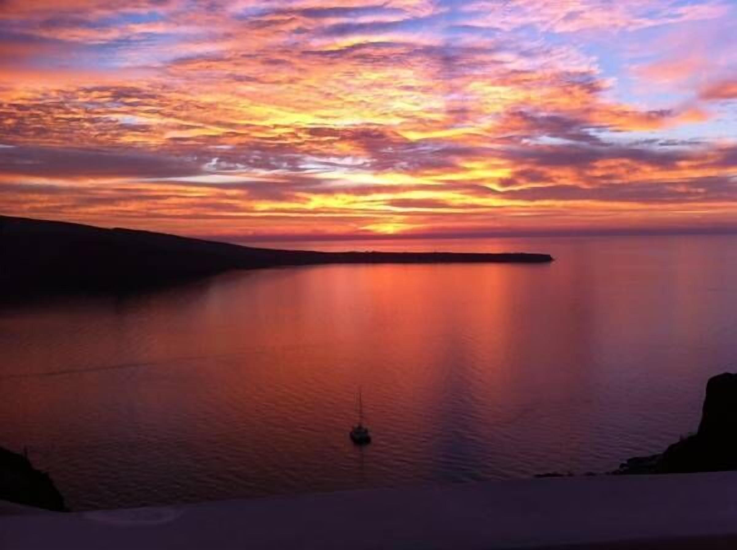 A sunset over a calm sea with a small boat anchored in the middle.