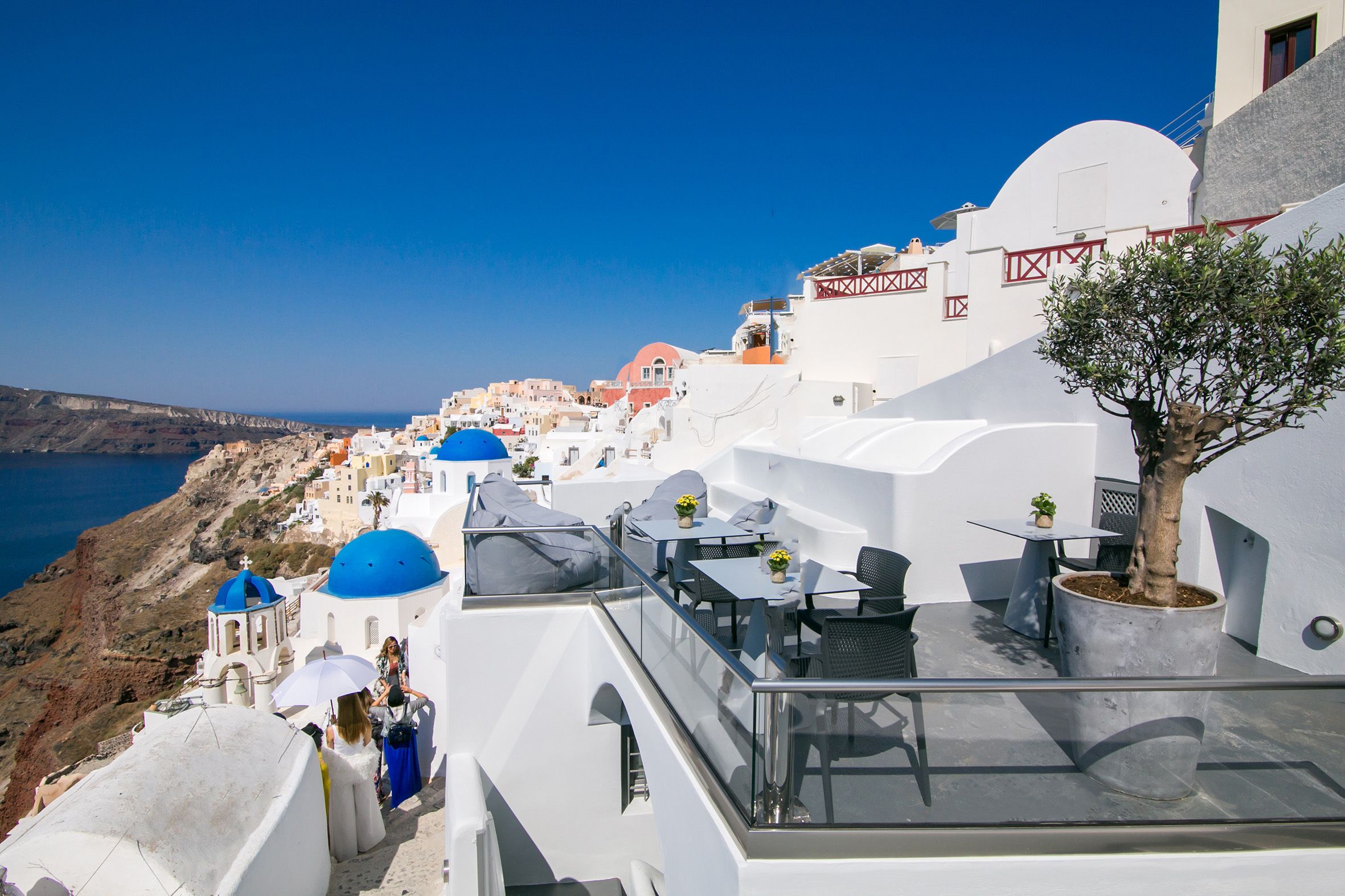 A rooftop terrace with outdoor seating, a potted tree, and a view of the coastline.