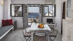 A room with a table set for two, a sofa, and a view of the sea.