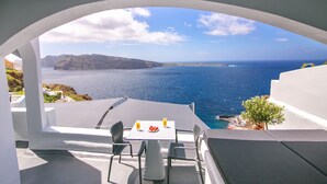 A terrace with a table and chairs, overlooking a coastal view with the sea and distant land.