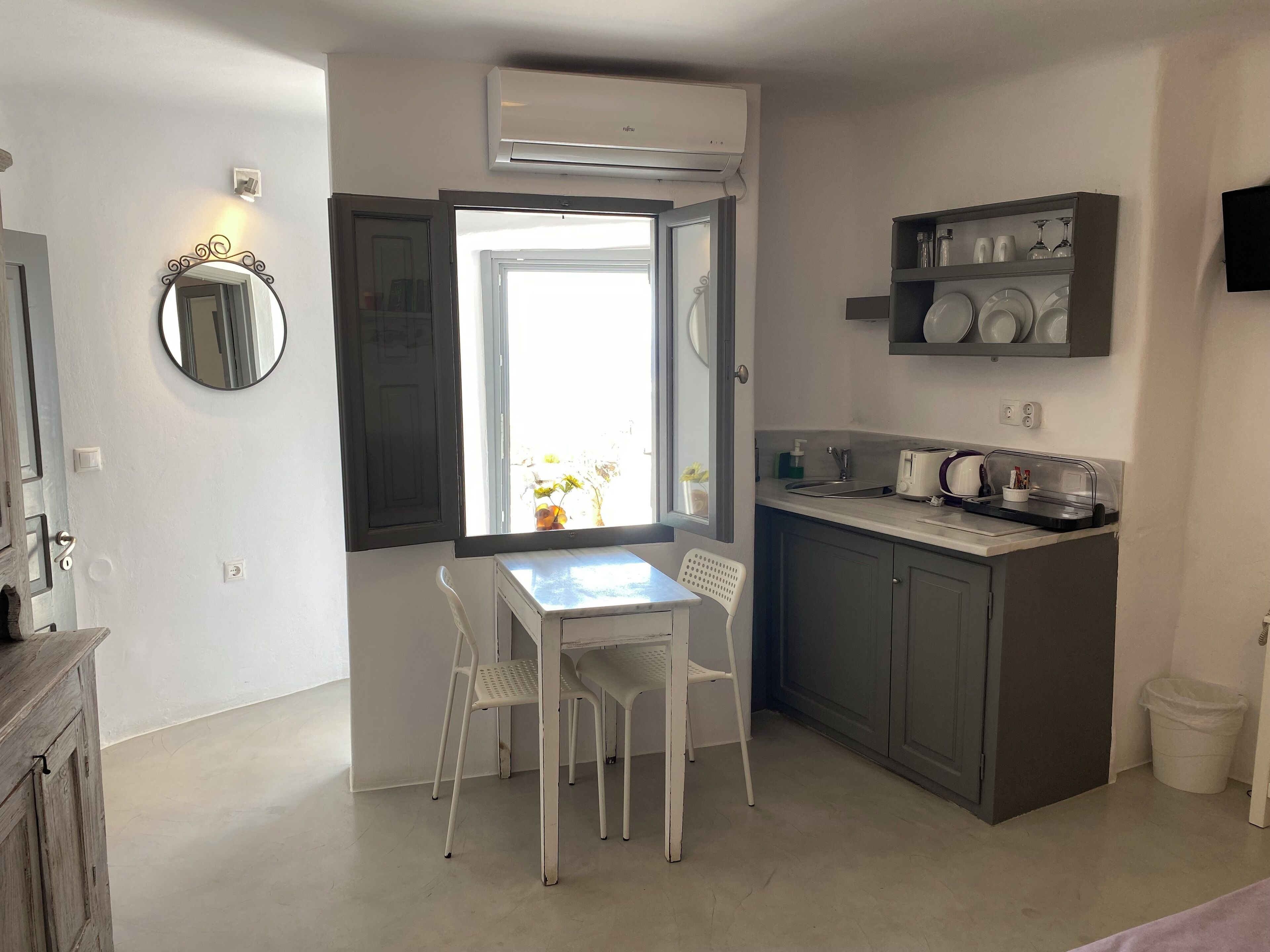 A compact kitchen with a dining area, featuring a white table and chairs, a built-in sink, and a shelf with dishes.