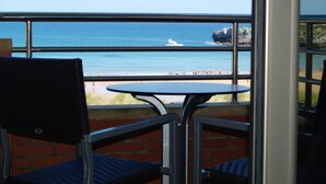 A balcony with a table and chairs overlooking a beach with people and a boat. - Hotel Marítimo Ris (Noja)