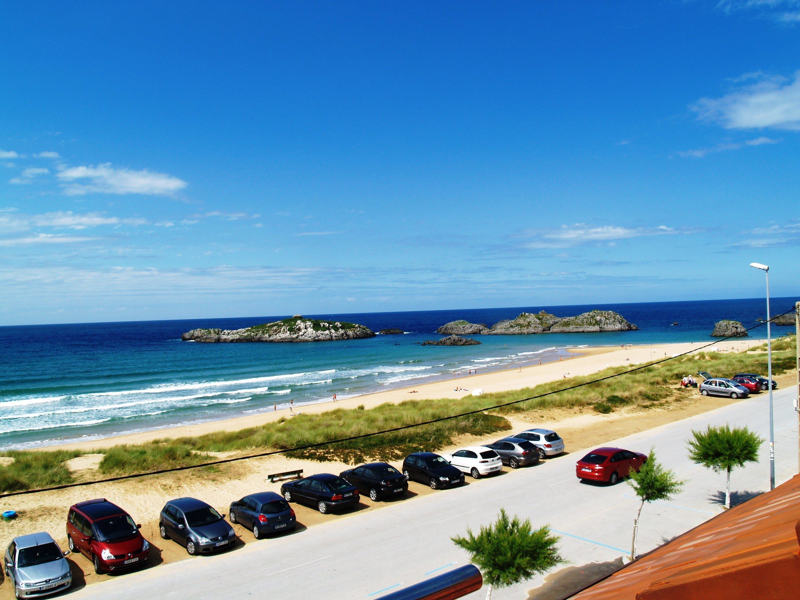 Un estacionamiento con coches y una playa al fondo.