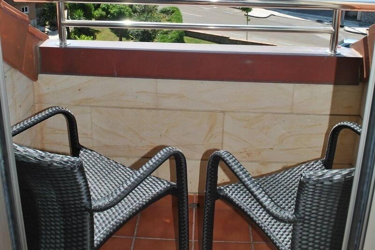 A balcony with wicker chairs, a metal railing, and a view of residential buildings in the background.