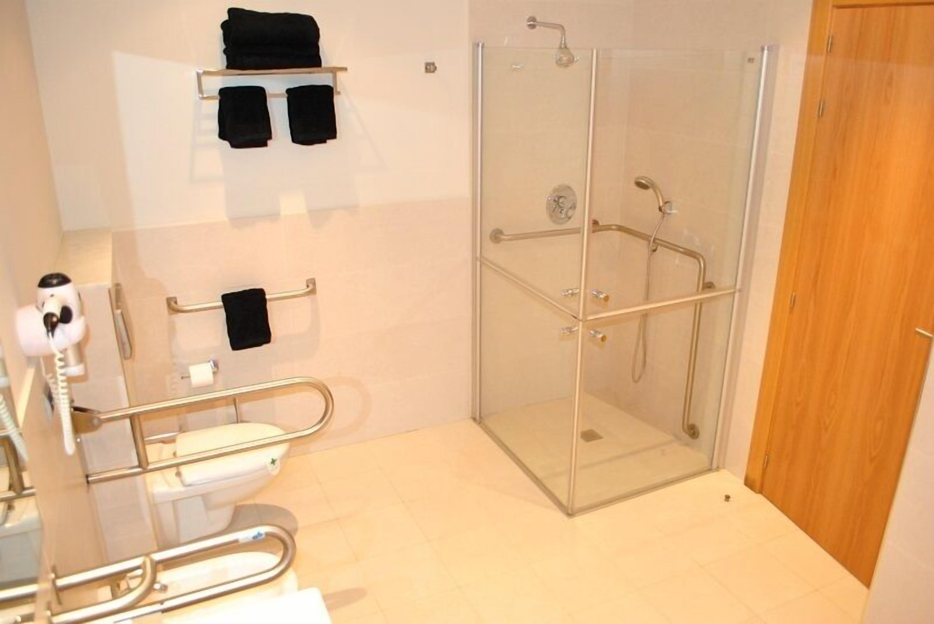 A bathroom with a glass-enclosed shower, a toilet with a grab bar, and a shelf with towels.