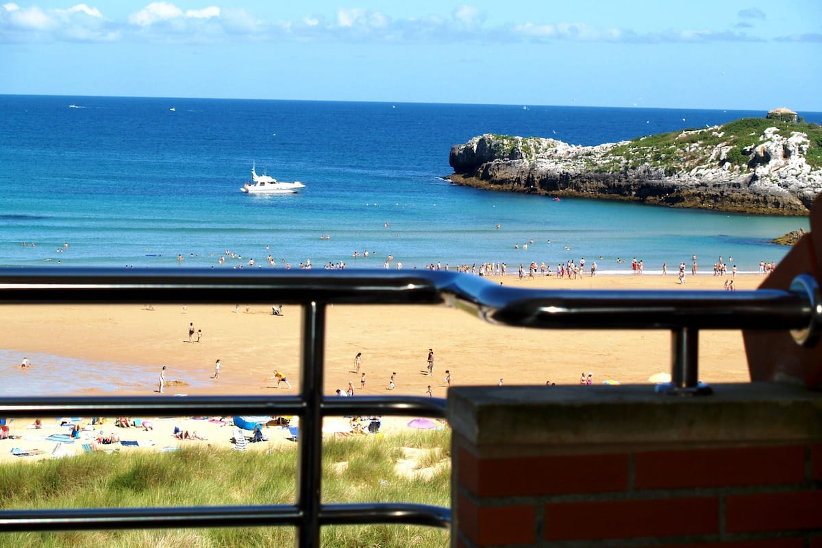 A beach with a view of the ocean, a boat, and rocky cliffs.