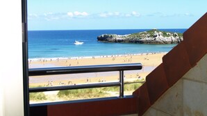 A view from a window overlooking a beach with a rocky outcrop and a boat on the water. - Hotel Marítimo Ris (Noja)