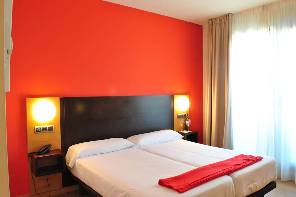 A hotel room with a large bed, two bedside tables, a nightstand, and a red throw blanket.