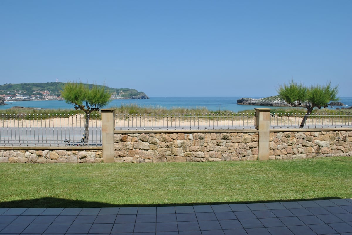 A coastal view with a stone wall, two trees, and a paved area in the foreground.