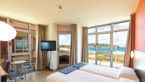 A hotel room with two beds, a TV, a balcony with a view of the beach, and a dining area. - Hotel Marítimo Ris (Noja)