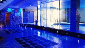 A modern indoor swimming pool with glass walls, a tiled floor, and a staircase leading to an upper level. - Hotel Marítimo Ris (Noja)
