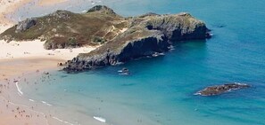 A coastal landscape with rocky outcrops, a sandy beach, and clear blue waters.