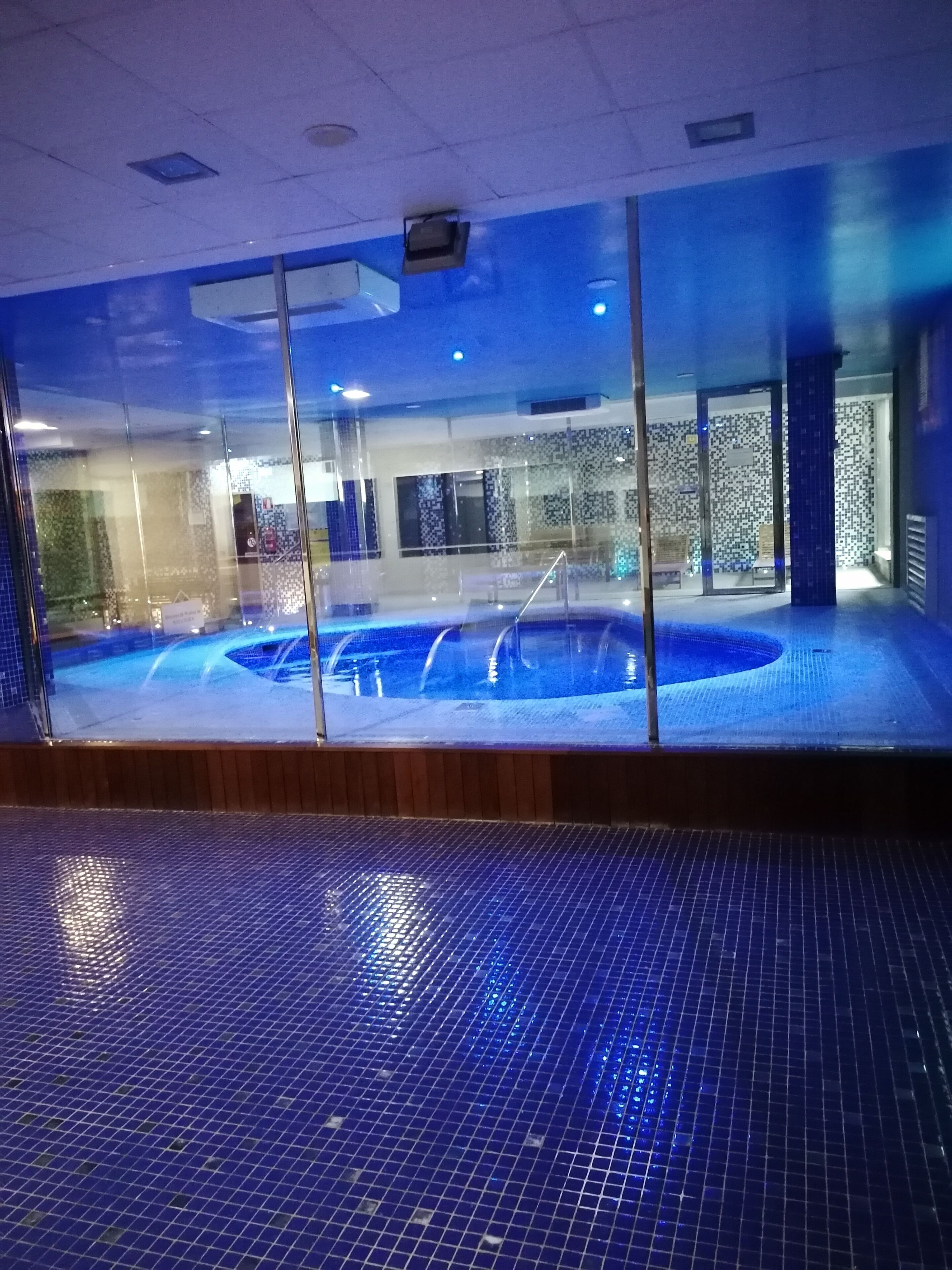 Una piscina interior con suelo de baldosas y paredes de cristal.