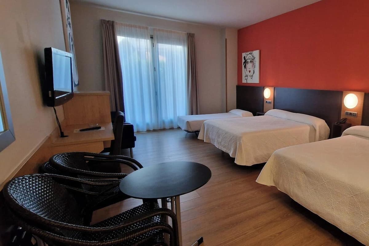 A hotel room with two beds, a desk, a chair, a TV, and a lamp.