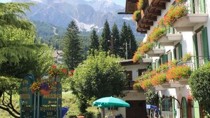 Hotel con vistas a la montaña, con balcones decorados con flores, un cartel con indicaciones y un paraguas verde.