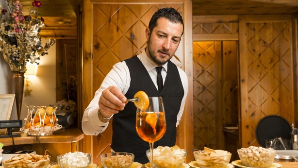 Una persona sirviendo una bebida adornada con una rodaja de naranja.
