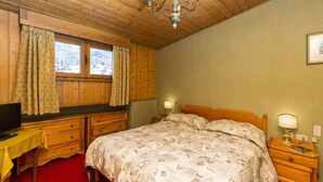 Un dormitorio con techo de madera, una cama con ropa de cama estampada, un escritorio con computadora y una ventana con cortinas.