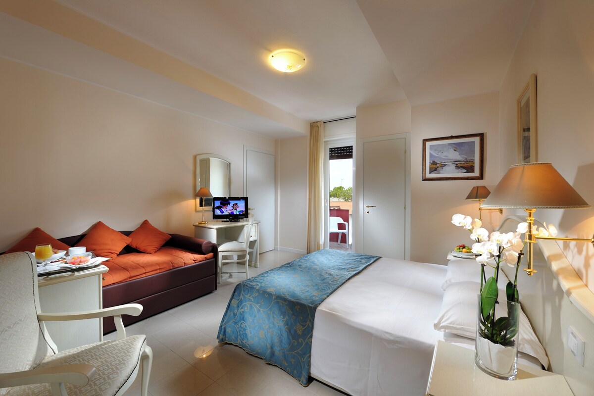 Une chambre d’hôtel comprenant un lit, un bureau avec un ordinateur, un canapé et un fauteuil.