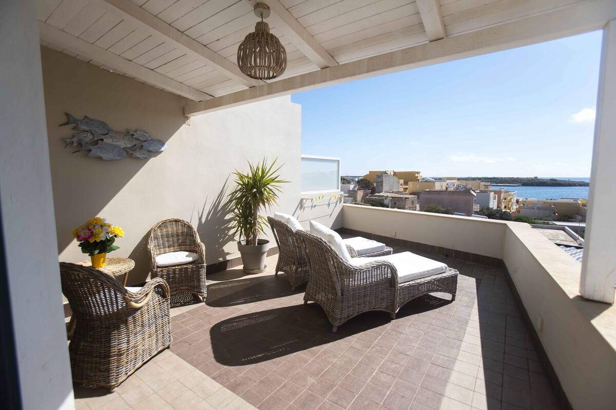A balcony with wicker furniture, a potted plant, and a view of the sea.