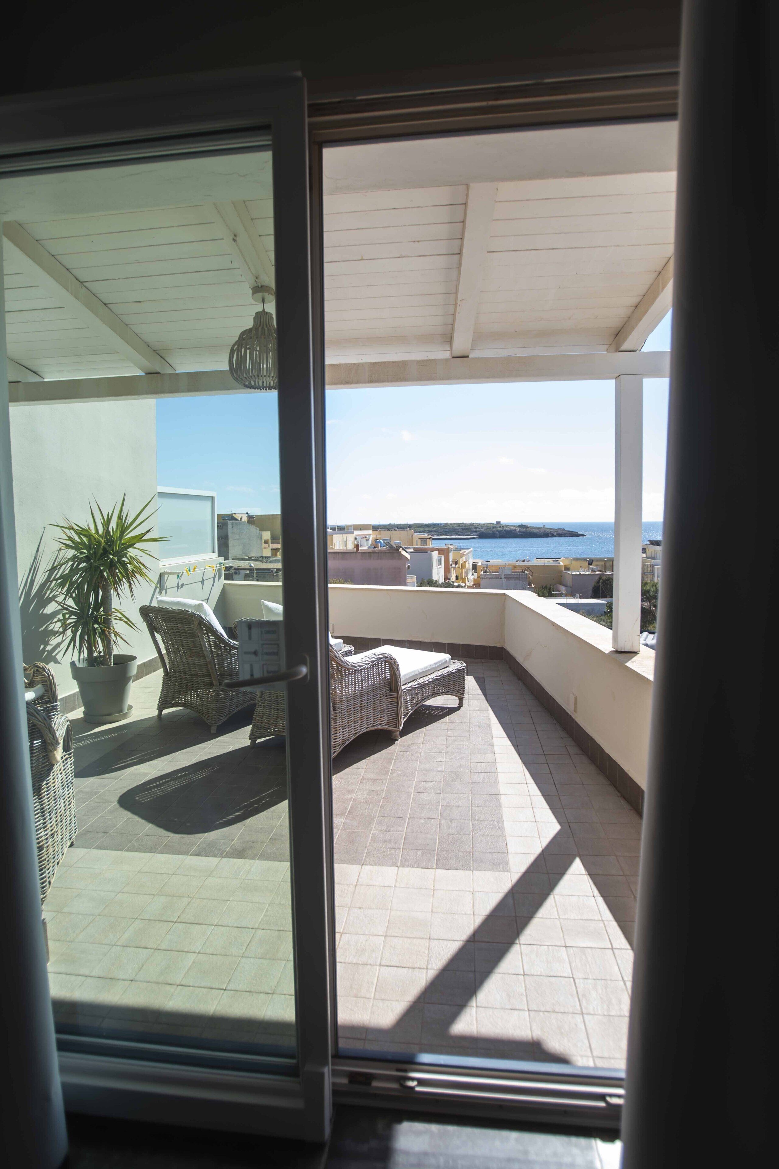 A balcony with wicker furniture, a potted plant, and a view of the sea.