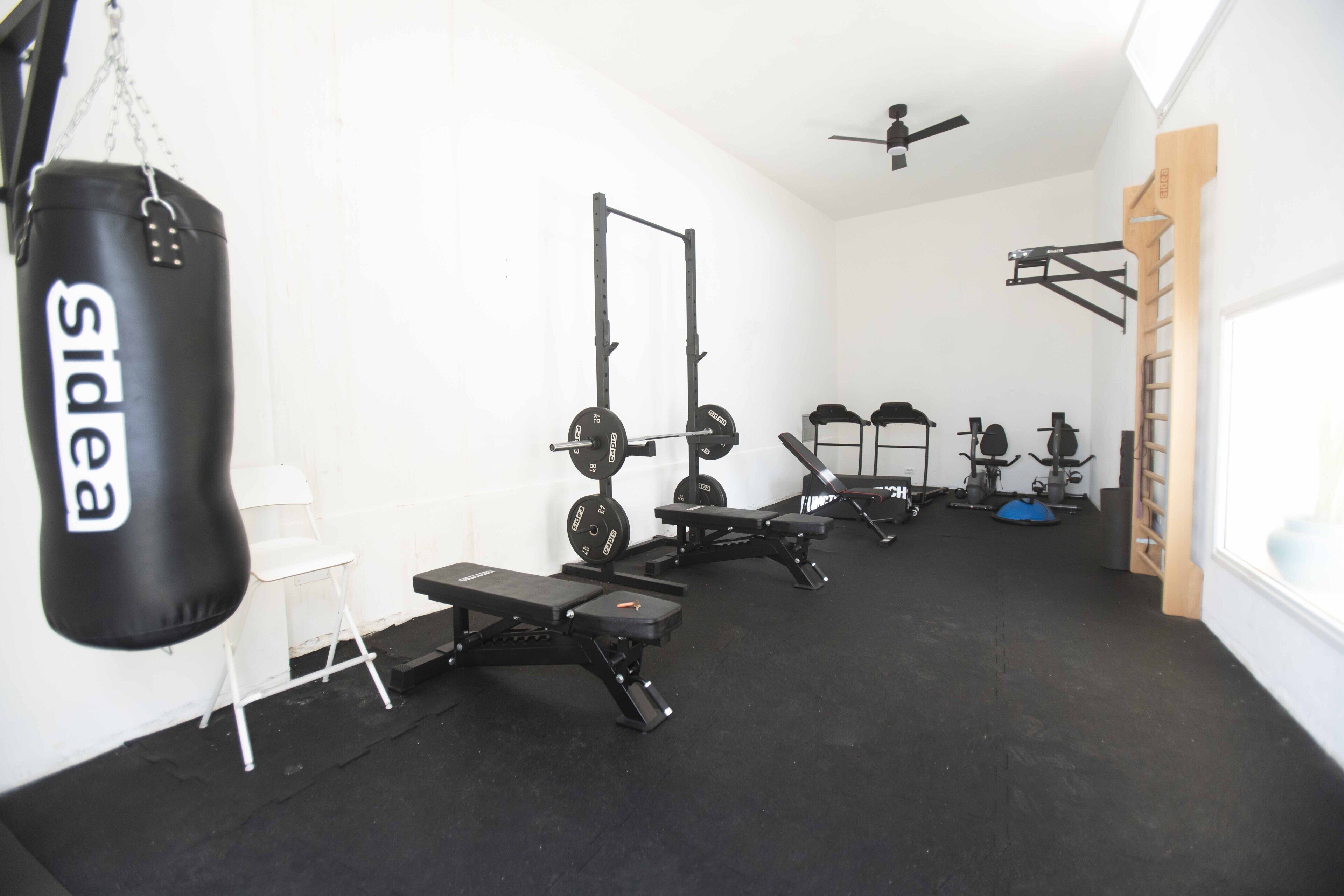 A gym with a punching bag, weight benches, a squat rack, and a pull-up bar.
