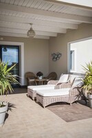 Un patio iluminado por el sol con muebles de mimbre, una planta en maceta y un adorno en la pared.
