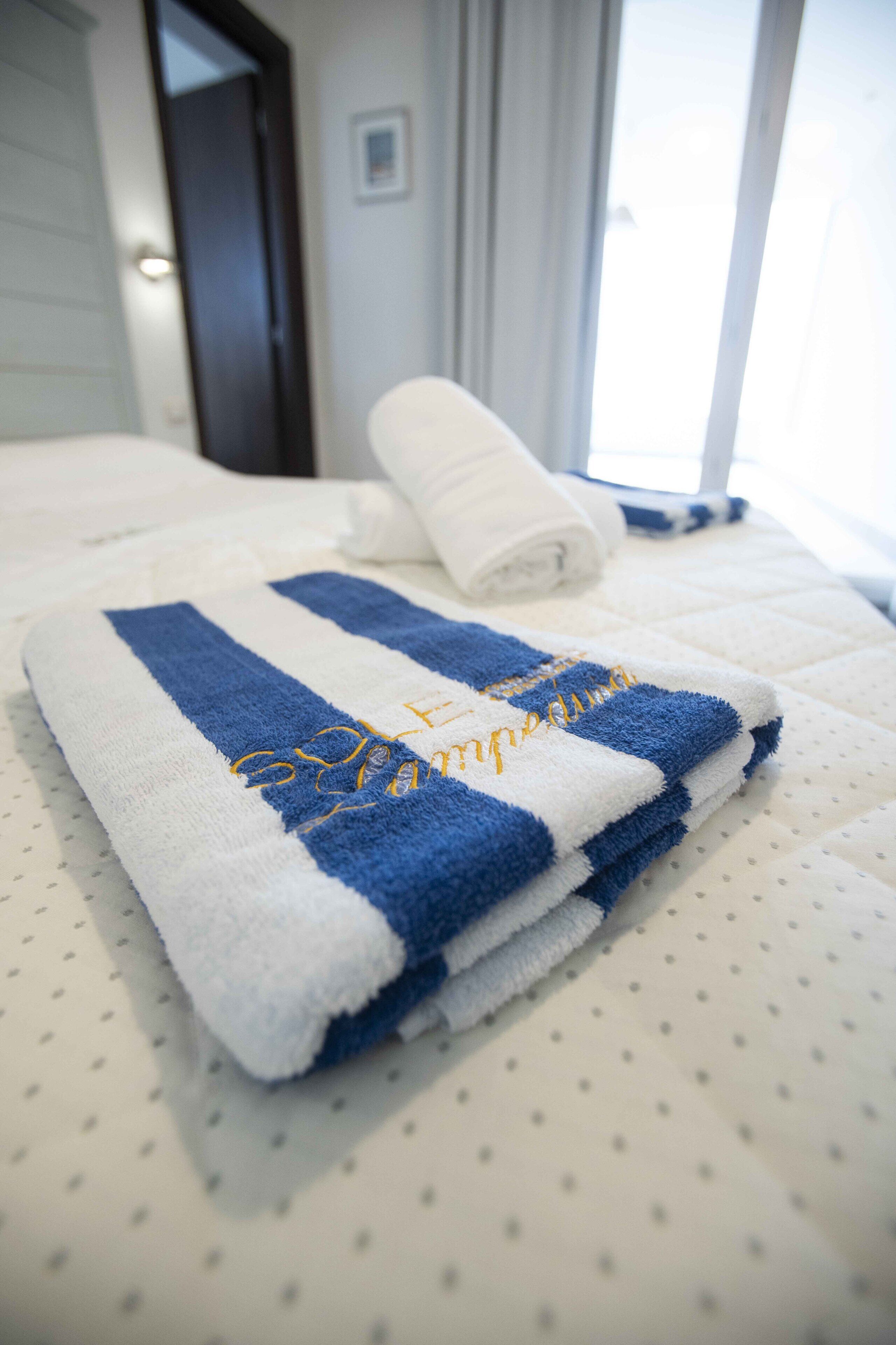 A neatly folded blue and white towel with embroidered text on a bed with a dotted pattern.